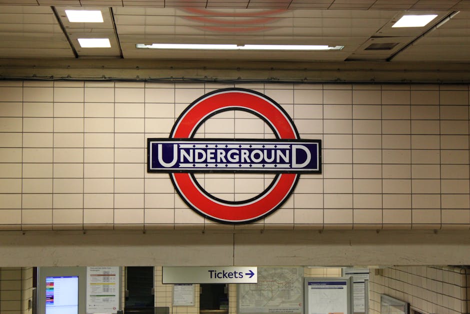 Nighttime view of Harrow & Hill underground station platform with brick walls and illuminated signage. In the foreground, train tracks run parallel to the platform edge, which has yellow safety lines.